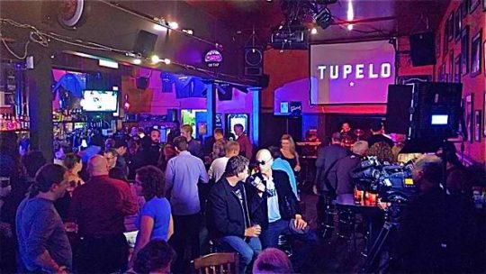 A crowd of people in a bar with microphones.