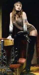 A woman in a dress and gloves standing on a bike.